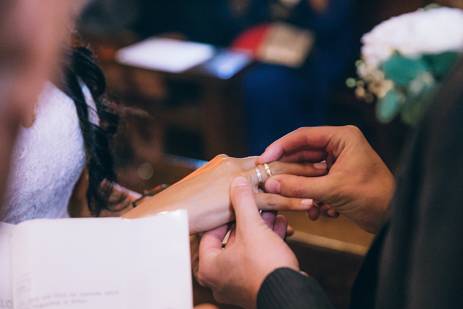 Person placing a ring on another person's finger, likely at a wedding or formal event.