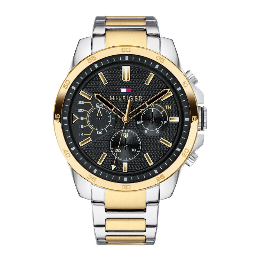 The Tommy Hilfiger Decker 1791559 WATCH features a silver and gold stainless steel band, black textured dial with gold accents, and three subdials.