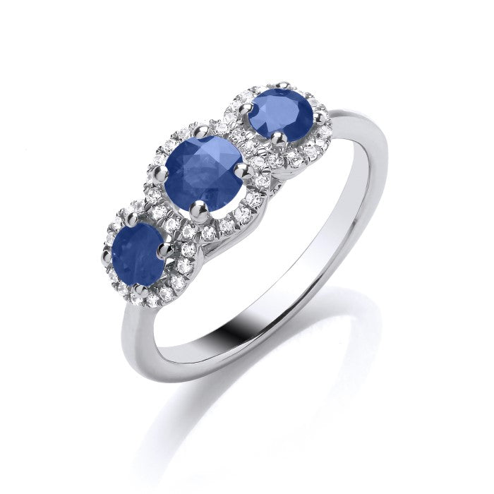 The 9ct White Gold Diamond and Sapphire Trilogy Ring showcases three round sapphires, each surrounded by sparkling diamonds and set in a sleek white gold band.