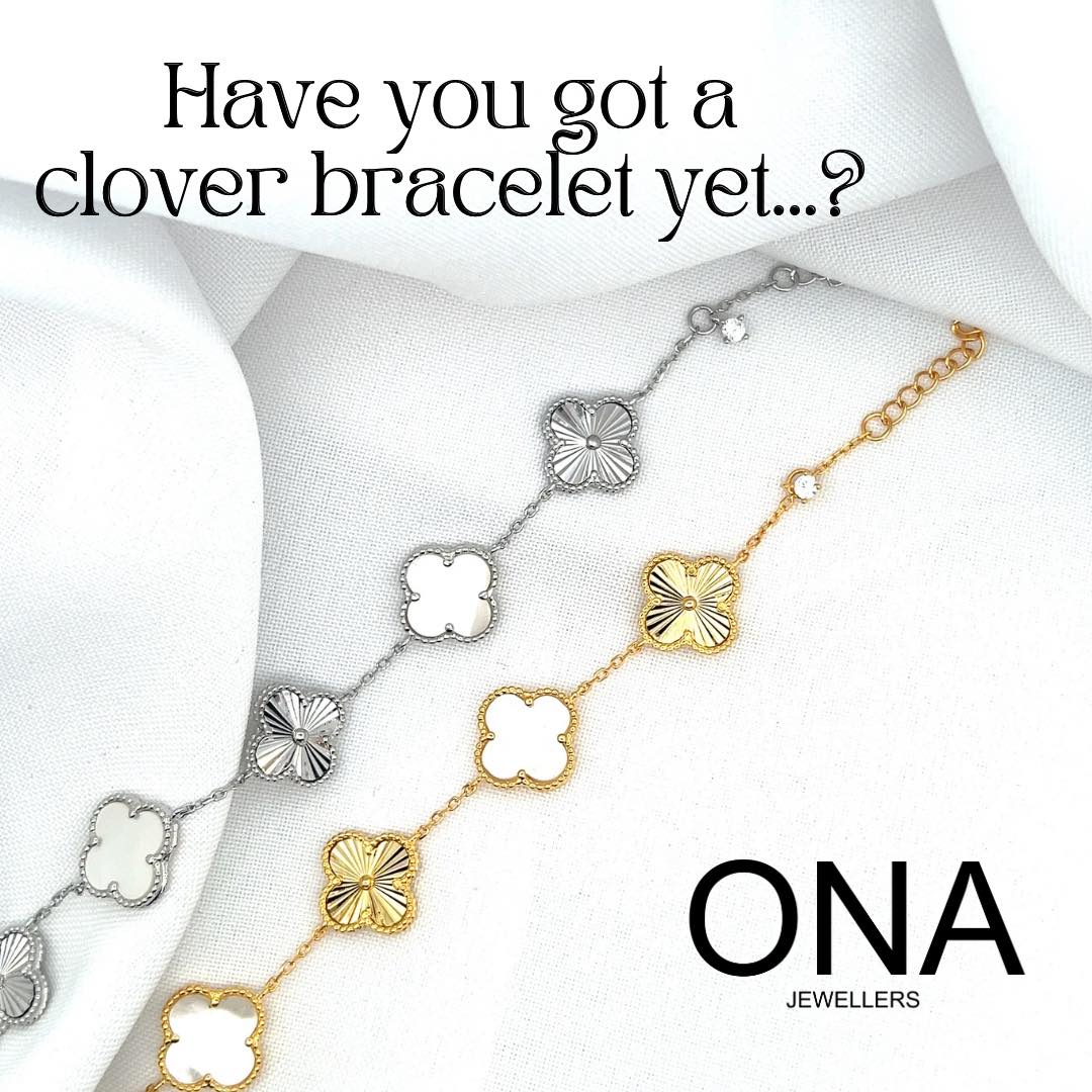 Two metal clover-shaped bracelets, one silver and one gold, displayed on a white fabric background with the text "Have you got a clover bracelet yet...? ONA Jewellers.