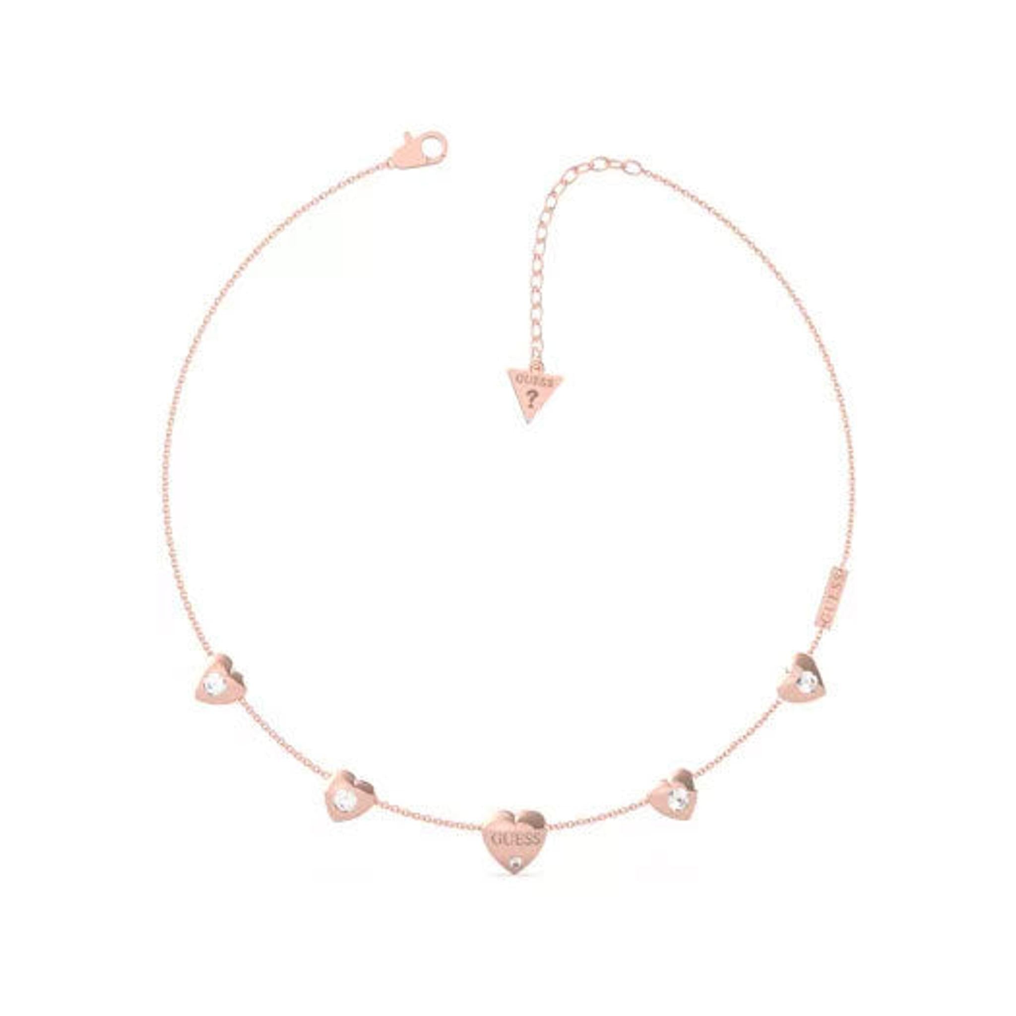 The GUESS JEWELLERY "GUESS IS FOR LOVERS" Rose Gold Tone Necklace UBN70030 features a thin chain with five small heart pendants (one engraved with "GUESS"), an adjustable clasp, and the signature GUESS triangle tag.