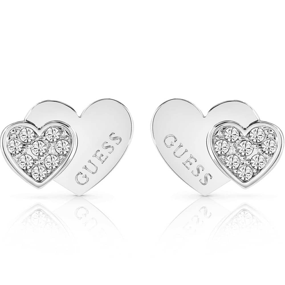 The Guess Me And You Crystal Double Heart Stud Earrings UBE84118 feature two silver heart shapes, each engraved with "GUESS" and accented by an overlapping Swarovski crystal heart.
