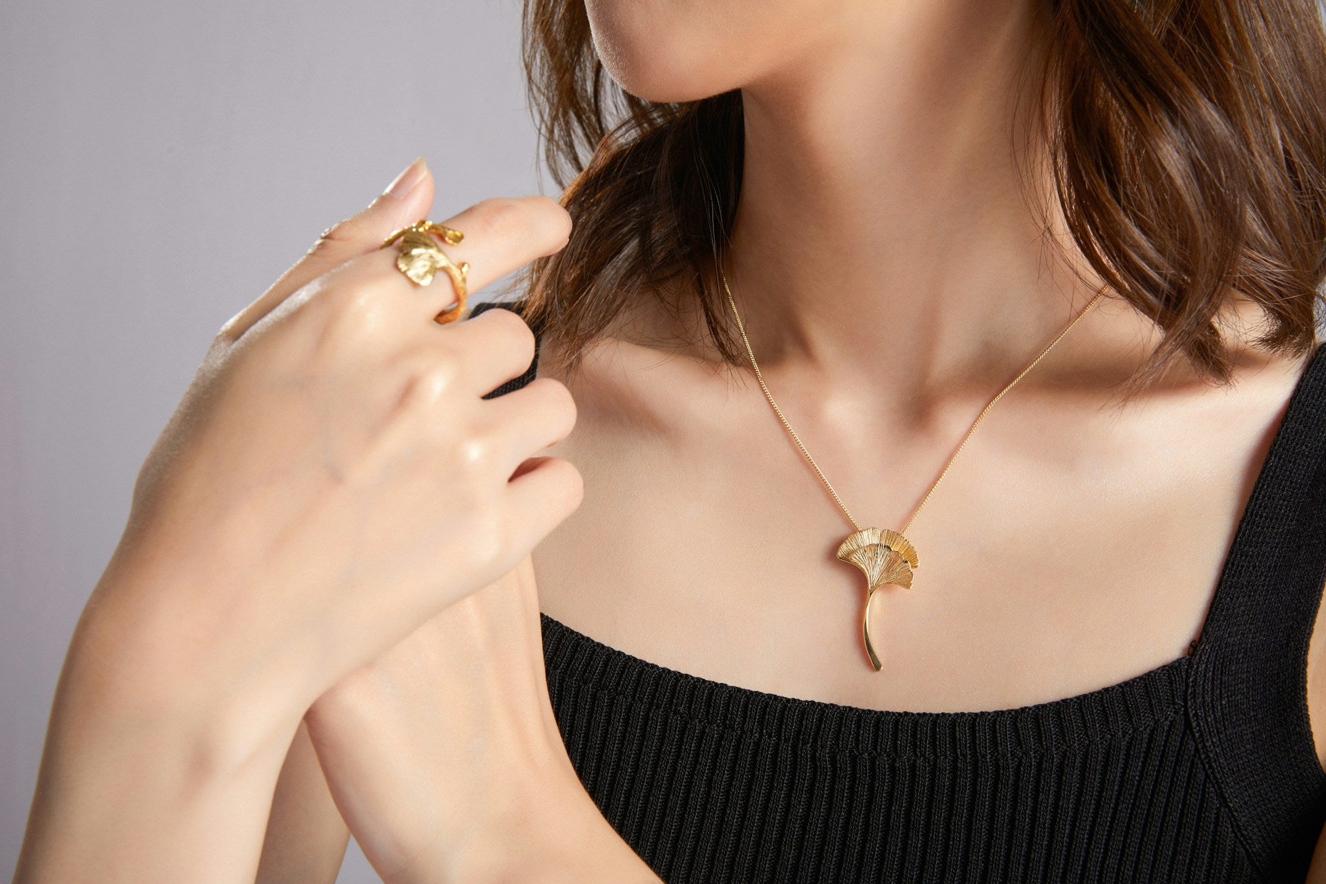 Woman wearing a gold necklace and ring against a neutral background