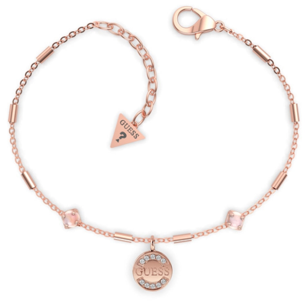 The Guess UBB79131-L Rose Gold Tone Nature Ladies Bracelet features a circular "GUESS" charm, sparkling Swarovski crystals, a lobster clasp, and a small triangular Guess logo tag.