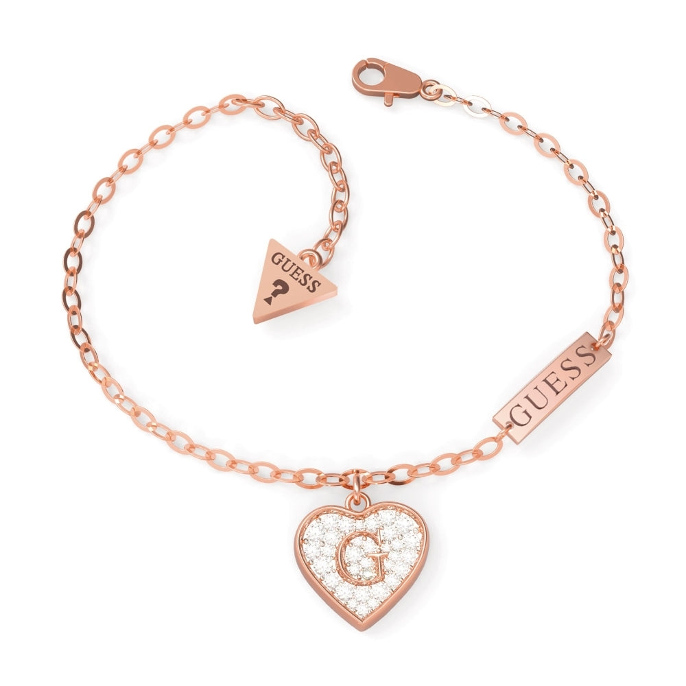 The Guess G Shine Rose Gold Plated Crystal Heart Bracelet (UBB79064-L) features a crystal heart-shaped pendant with a central "G" and two "GUESS" tags.