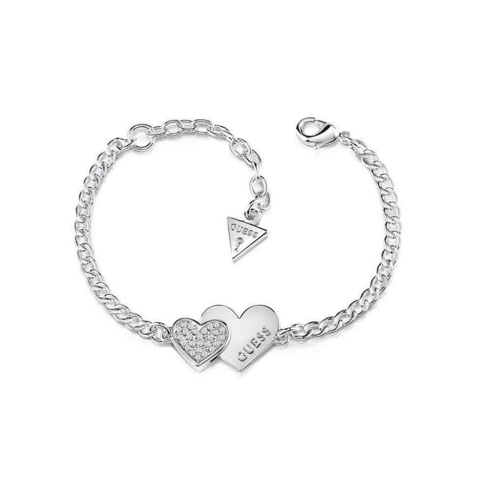 The GUESS UBB84123-L Silver Tone Me & You Double Heart Bracelet features two heart charms—one with Swarovski crystals, the other engraved with the Guess logo—and a small triangular GUESS tag by the clasp.