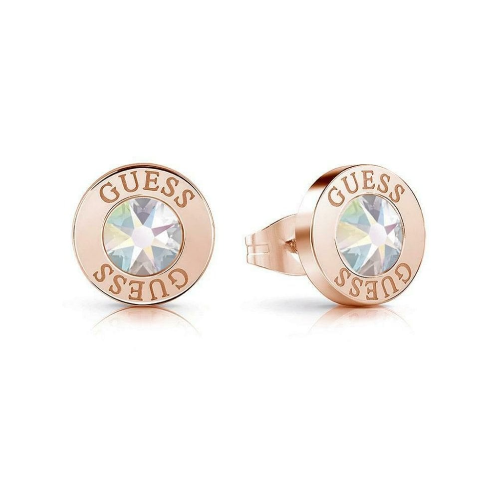 The GUESS UBE78096 Rose Gold Tone Shiny Crystals Aurora Stud Earrings feature round rose gold studs with clear crystal centers and "GUESS" engraved around the edge—an elegant addition to any outfit.