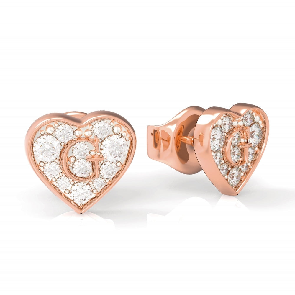 The Guess G-Shine Rose Gold Tone Swarovski Crystal Earrings (UBE79074) feature heart-shaped studs adorned with sparkling crystals and a prominent letter "G" at the center.