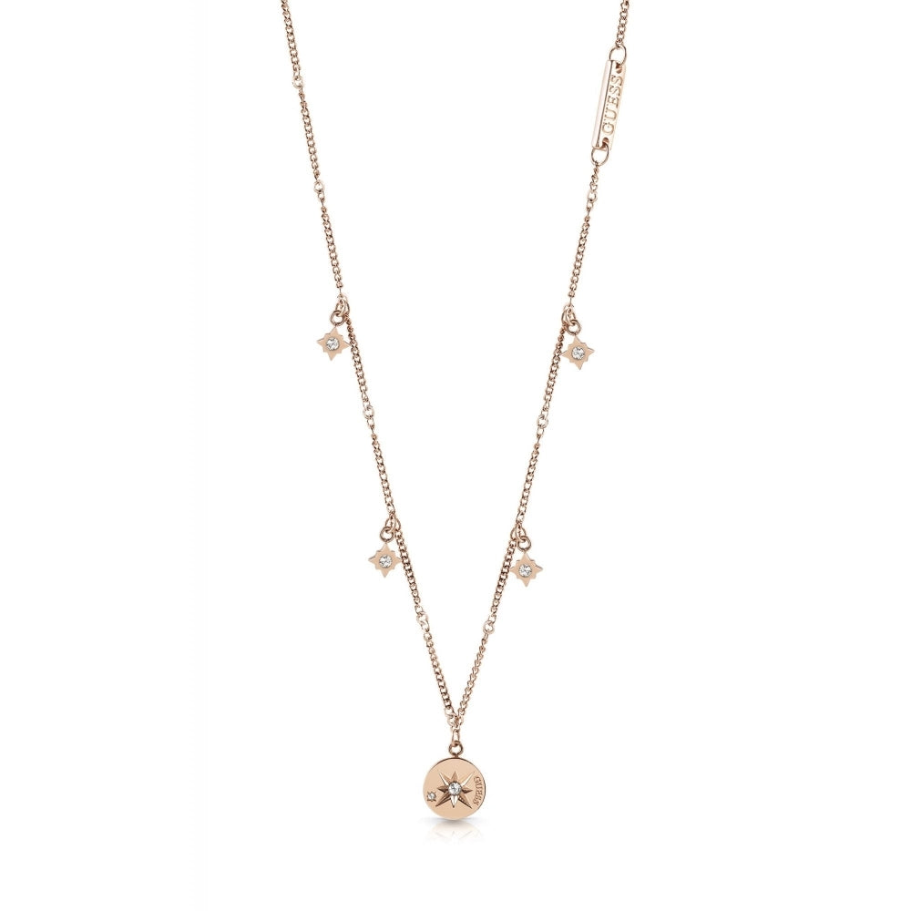The Guess UBN20029 Wanderlust Rose Gold Tone Crystal Set Compass and Charm Necklace features a delicate rose gold chain with four star charms and a central round compass pendant, each adorned with sparkling Swarovski crystals.