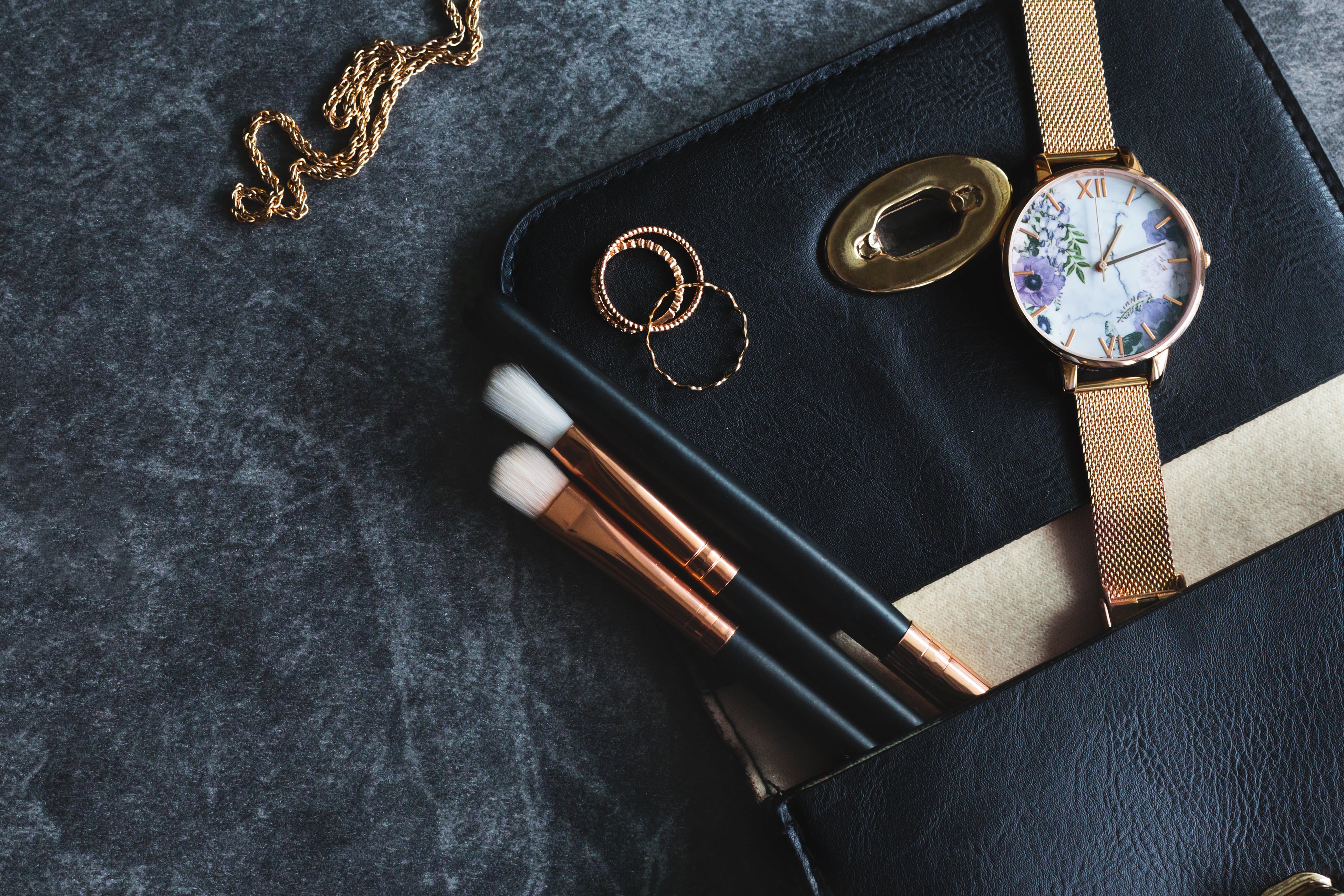 Make up brushes, rings, necklace and watch on top of a purse