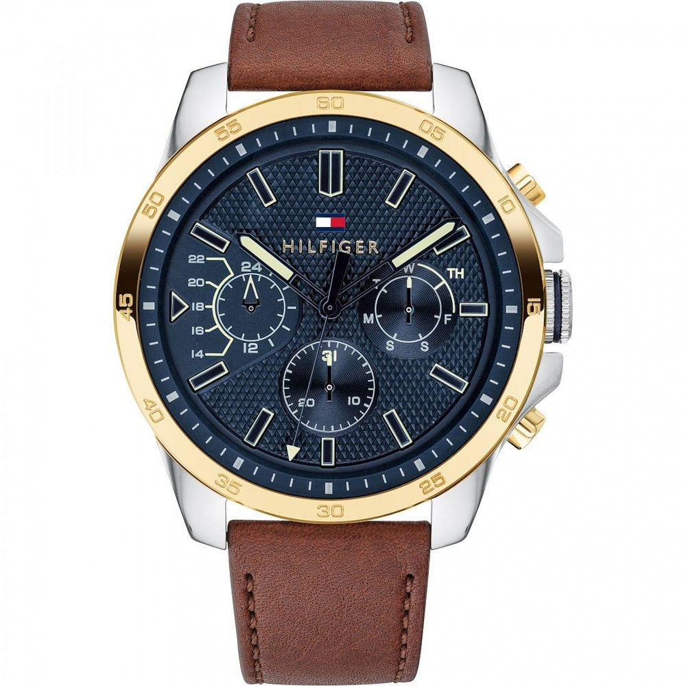 The Tommy Hilfiger 1791561 Men's Brown Leather Strap Wristwatch showcases a blue textured dial, gold bezel, multiple subdials, stainless steel case, and is finished with "Hilfiger" branding plus a small flag logo.