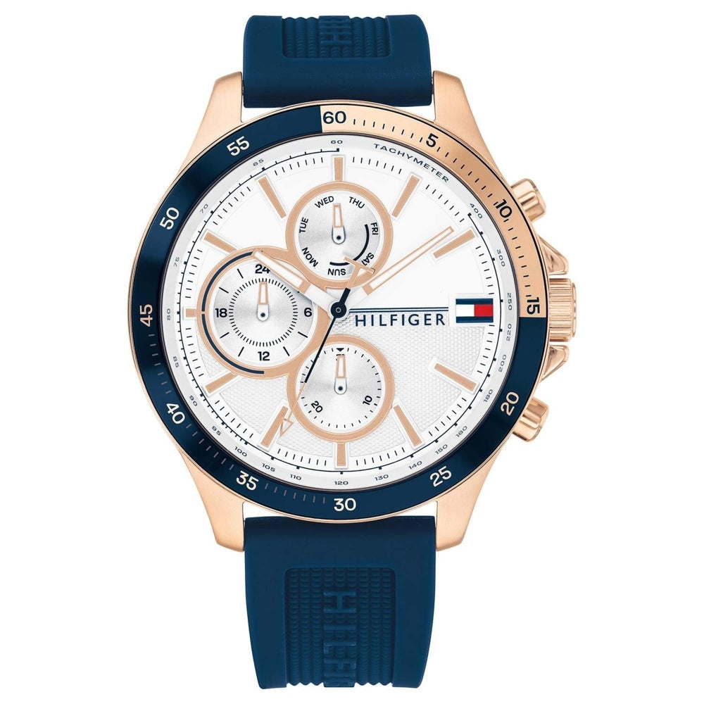 The Tommy Hilfiger 1791778 Men's Blue Silicone Strap Wristwatch features a rose gold-tone case, white dial with multiple subdials, and the iconic logo on the face.