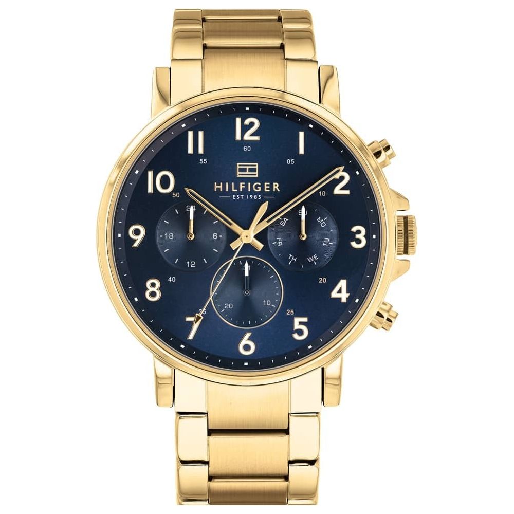 The Tommy Hilfiger 1710384 Stainless Steel Gold Tone Bracelet Men's Watch features a blue dial, gold hour markers, three subdials, and is displayed against a white background.