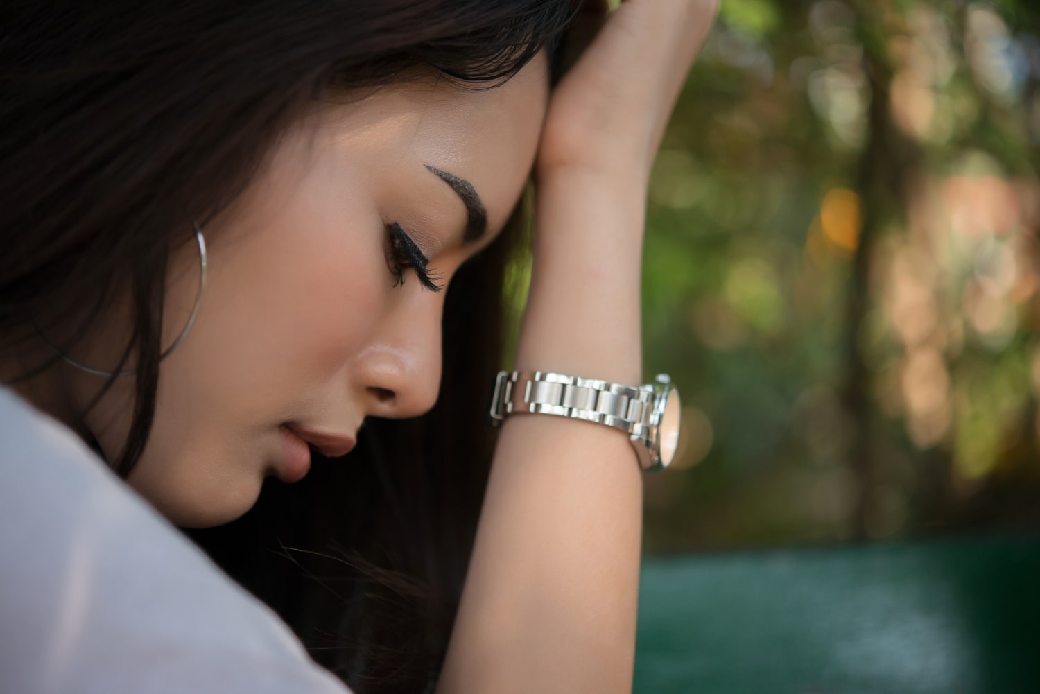 Woman with a silver watch on her wrist, looking down with a blurred natural background